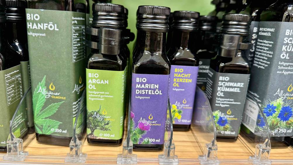 Mehrere Flaschen Mariendistelöl im Test neben anderen Produkten in einem Verkaufsregal.