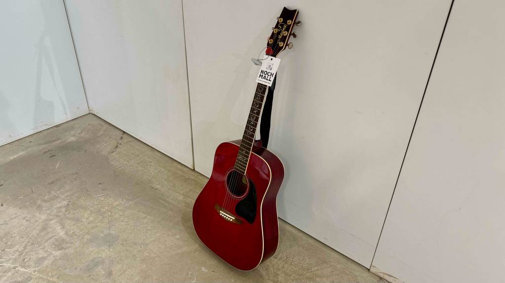 Eine bordeauxrote getestete 7-8-Gitarre im Test steht an einer weißen Wand.