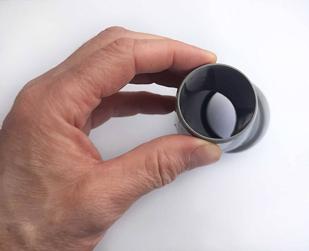 Eine Hand hält das graue, angewinkelte, getestete PVC-Rohr vor einem weißen Hintergrund.
