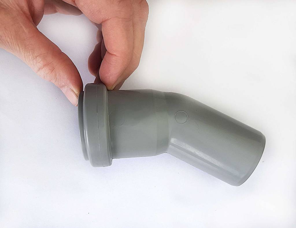 Die Hand zeigt den Muffen-Teil des grauen, angewinkelten PVC-Rohrs im Test.