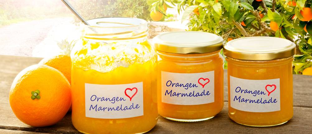 Marmeladenglas im Test: Beschriftete Gläser mit Orangenmarmelade stehen auf einem Holzuntergrund