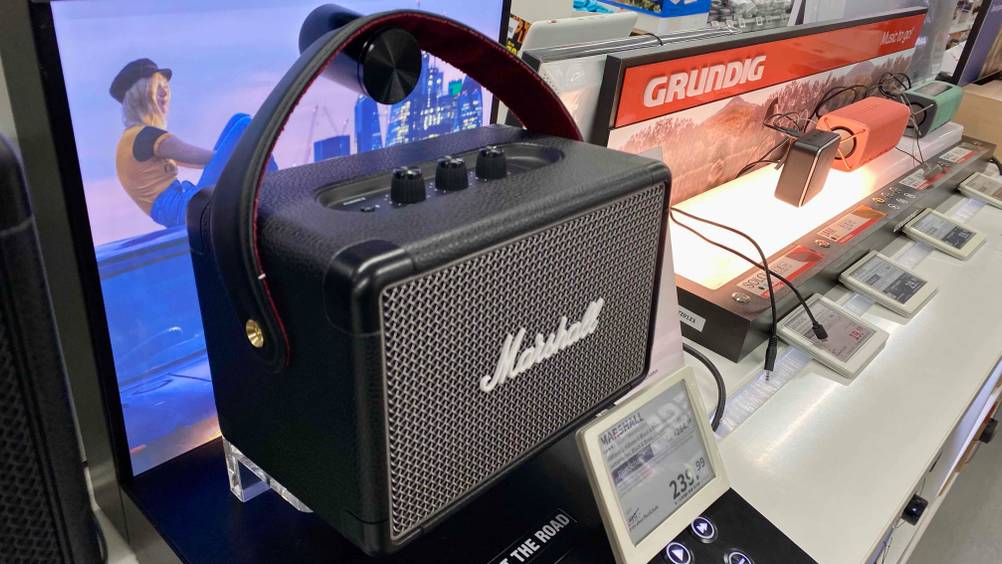 Ein getesteter Marshall-Bluetooth-Lautsprecher von schräg vorne in einer Verkaufsfläche neben anderen Produkten inklusive Preisschild.