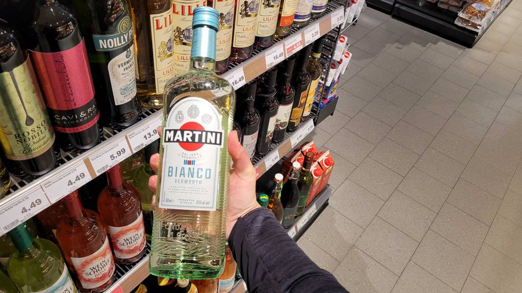 Weißer Wermut-Test: Eine Hand hält eine Flasche vor einen Verkaufsregal.