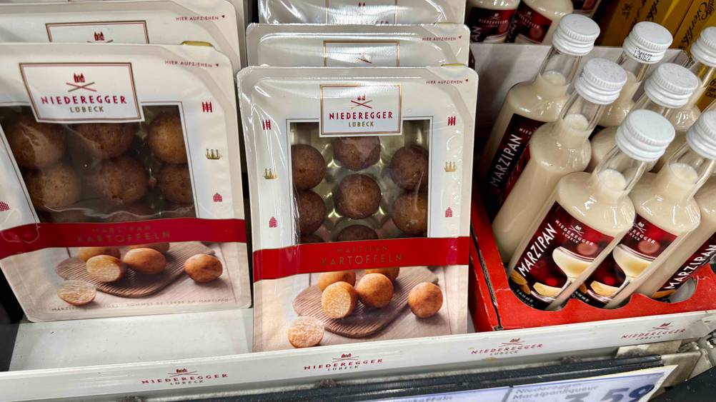 Mehrere Packungen der getesteten Marzipankartoffeln in einem Verkaufsregal neben anderen Produkten.