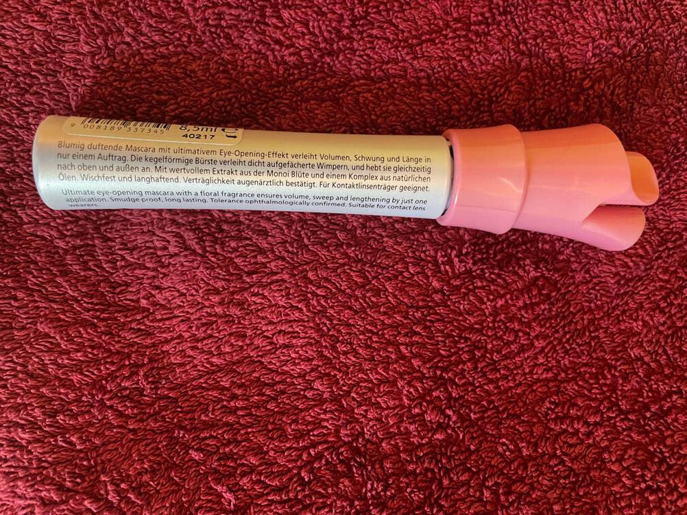 Rückseite einer Tube getesteter Mascara auf einem pinken Handtuch.