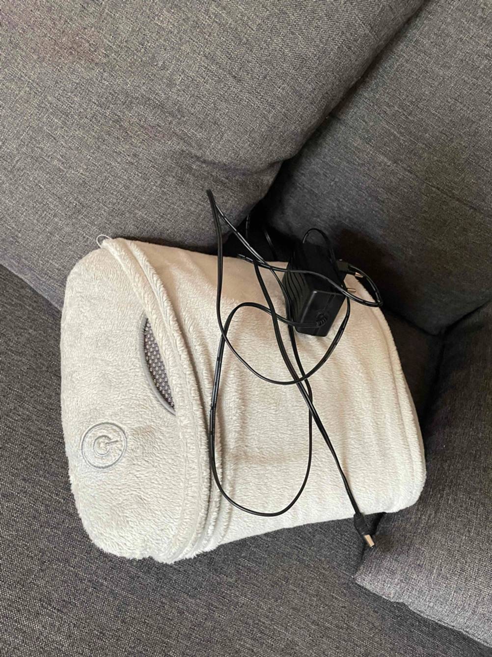 Verpackung und Ladekabel von einem getesteten Massagekissen liegen auf dem Sofa.