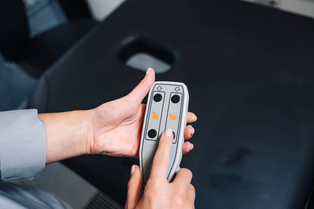 Massageliege-elektrisch-Test: Eine Frau bedient eine Elektro-Massageliege mittels Fernbedienung.