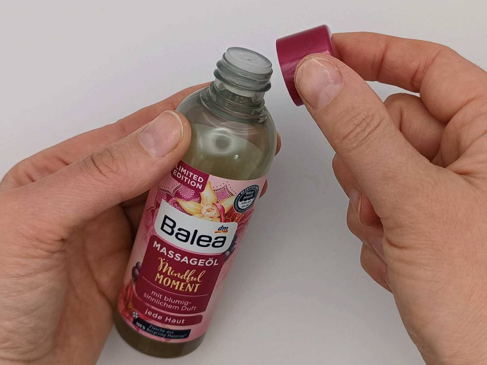 Eine Hand entfernt die Verschlusskappe an einer Flasche des getesteten Massageöls.