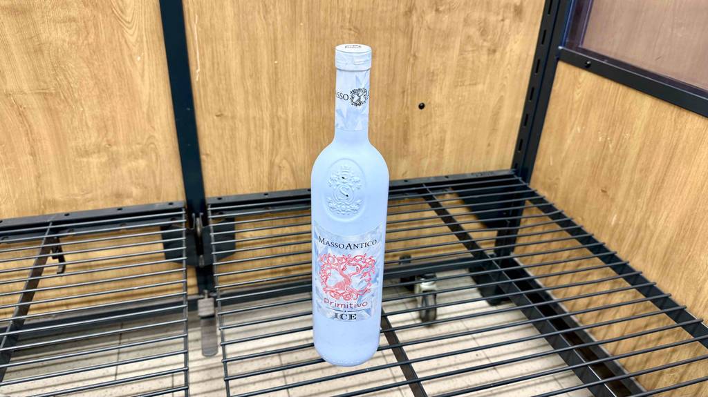 Blick von schräg oben auf eine Flasche Primitivo, die zum testen in einem Gitterregal steht.