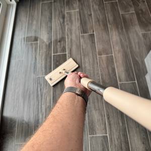 Eine Hand wischt mit dem Bodenwischer des Masthome-Wischmopp-Sets über einen Fliesenboden.