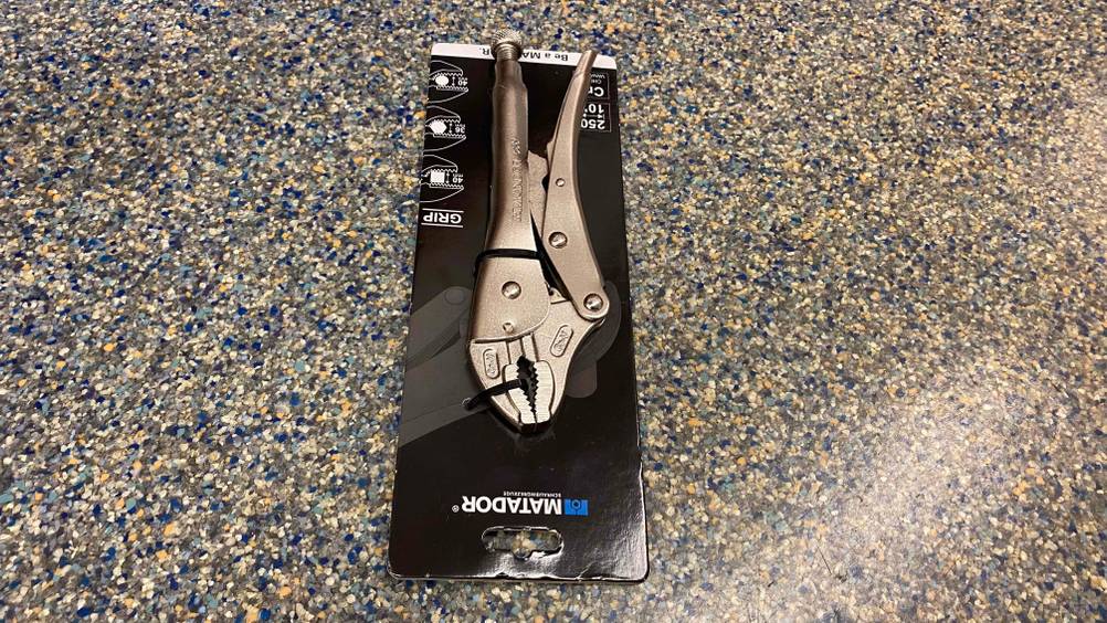 Eine getestete Gripzange in Originalverpackung auf den Kopf gedreht auf einem bunten Boden.
