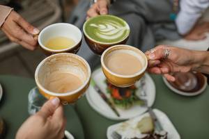 Matcha-Latte-Test: 4 Personen halten Tassen mit Matcha Latte und Kaffee in der Hand. 