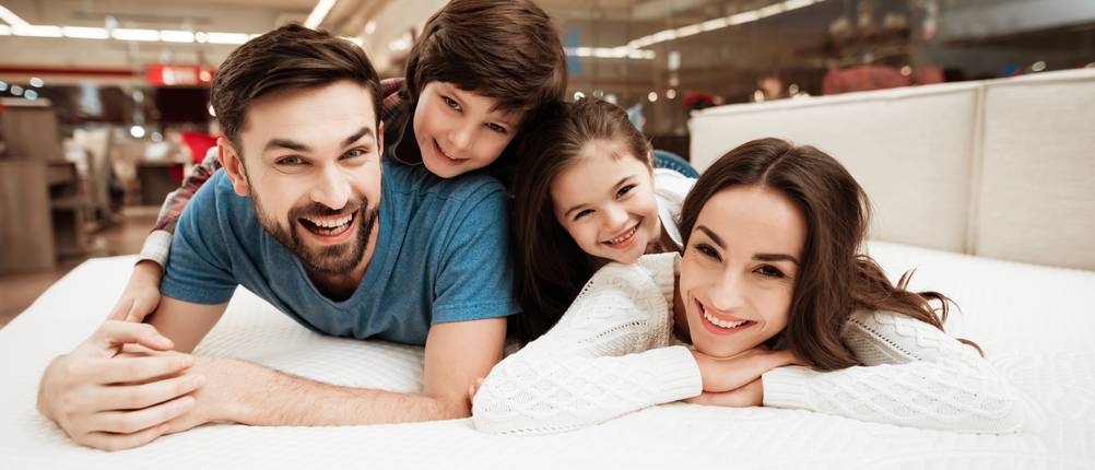 Matratze-180-x-200-Test: Zu sehen ist eine Familie mit zwei Kindern, die gemeinsam auf einer Matratze liegt und in die Kamera schaut.
