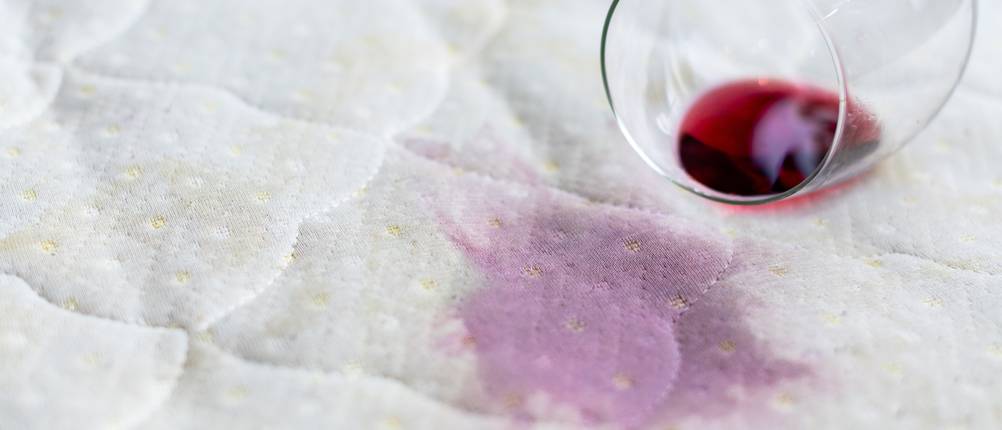 Matratzenschoner-120-x-200-Test: Ein Glas mit Rotwein liegt verschüttet auf einer Matratze.