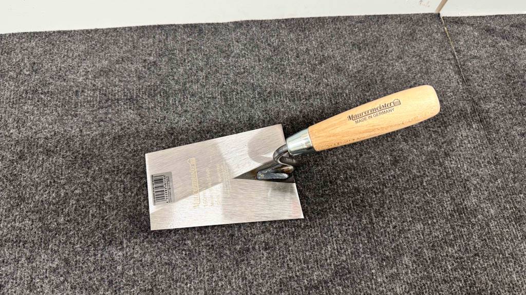 Die Maurerkelle im Test inklusive Holzgriff liegt auf einem grauen Teppichbelag.