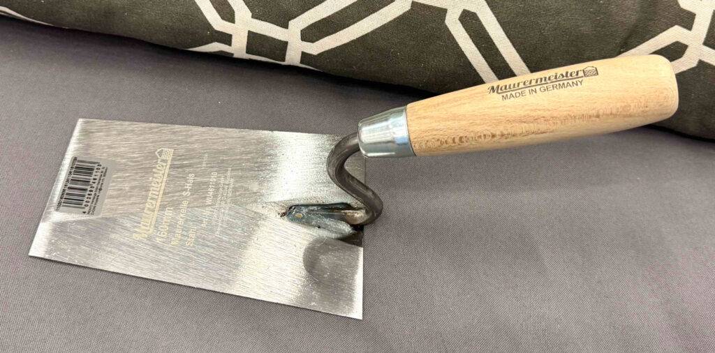 Im Test: Die Maurerkelle mit Holzgriff liegt auf einem grauen Stoff.