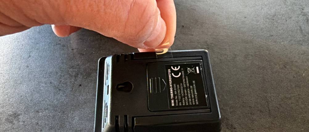 Eine Hand entfernt ein Stück Plastik von der Batterieabdeckung