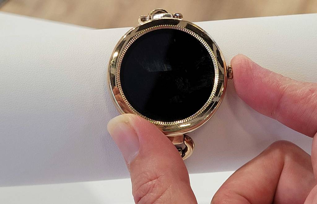 Hybrid Smartwatch im Test: Hand drückt Rädchen eines dunklen Ziffernblatts einer goldenen Maxcom Uhr.