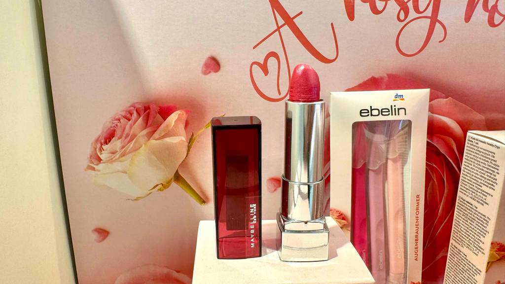Maybelline Lippenstift im Test: Ein geöffneter Lippenstift steht vor einer Wand mit Rosen.