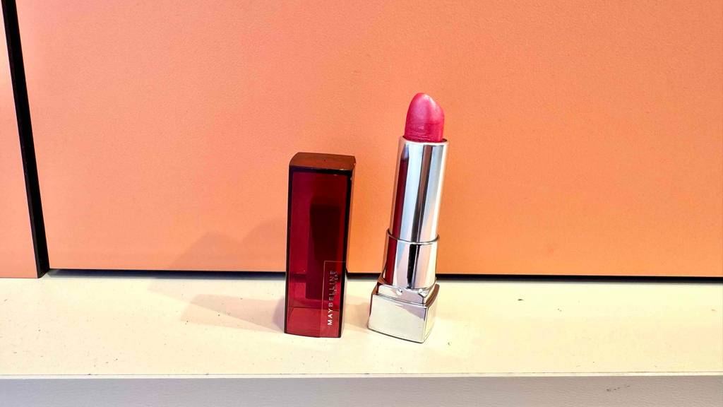 Ein getesteter Maybelline Lippenstift steht vor einer lachsfarbenen Wand, daneben die Kappe.