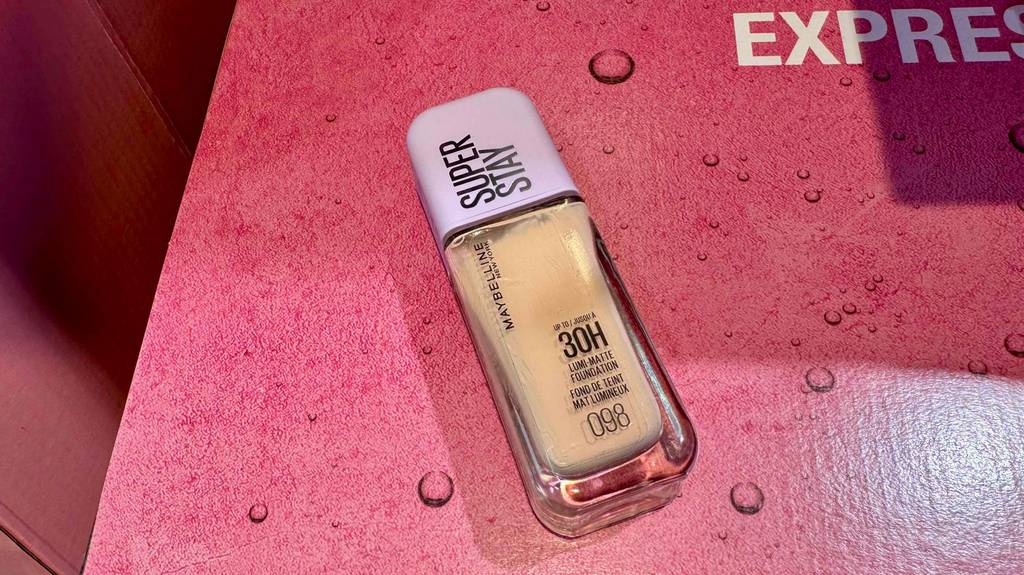 Im Test: Ein Fläschchen Maybelline-Foundation liegt auf einer roten Fläche mit Tropfendesign.