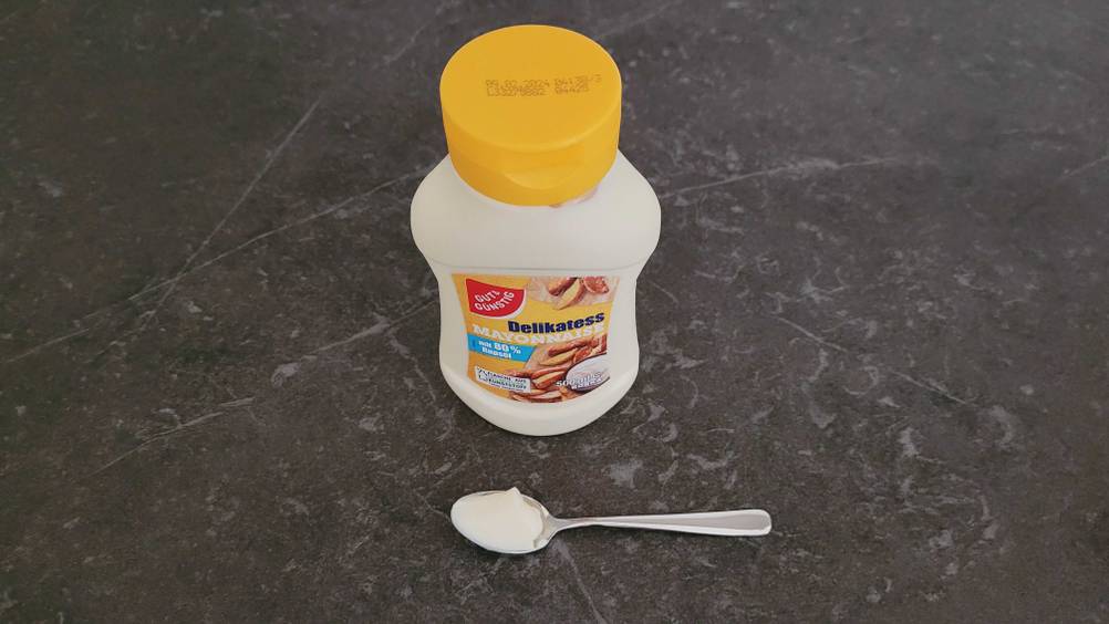 Mayonnaise getestet: Eine Flasche von oben mit einem Löffel davor auf einer dunklen Fläche.