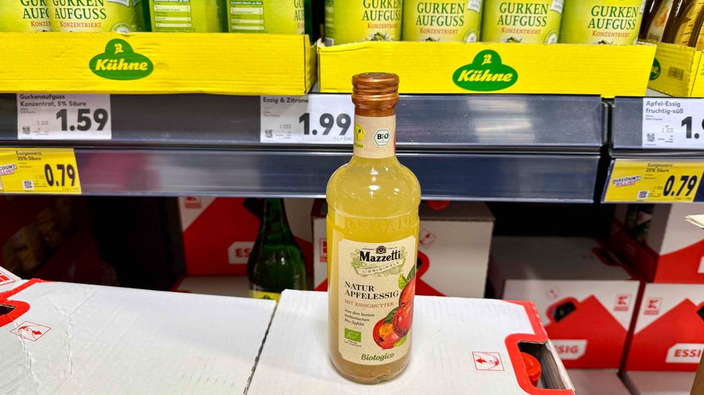 Eine Flasche getesteter Apfelessig naturtrüb steht auf einem Karton vor einem Verkaufsregal.