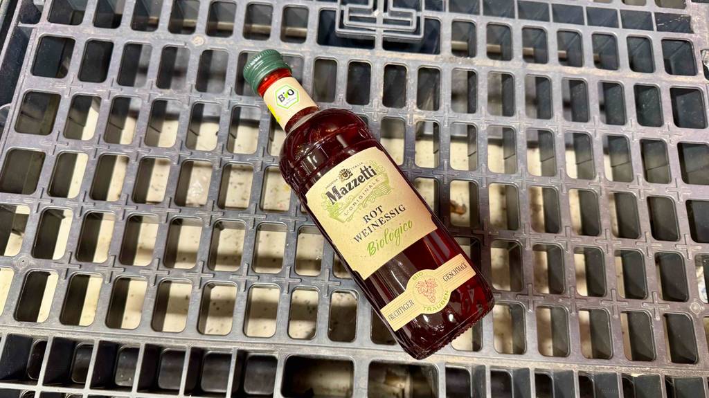 Eine Flasche getesteter Rotweinessig liegt auf einem Gitter.