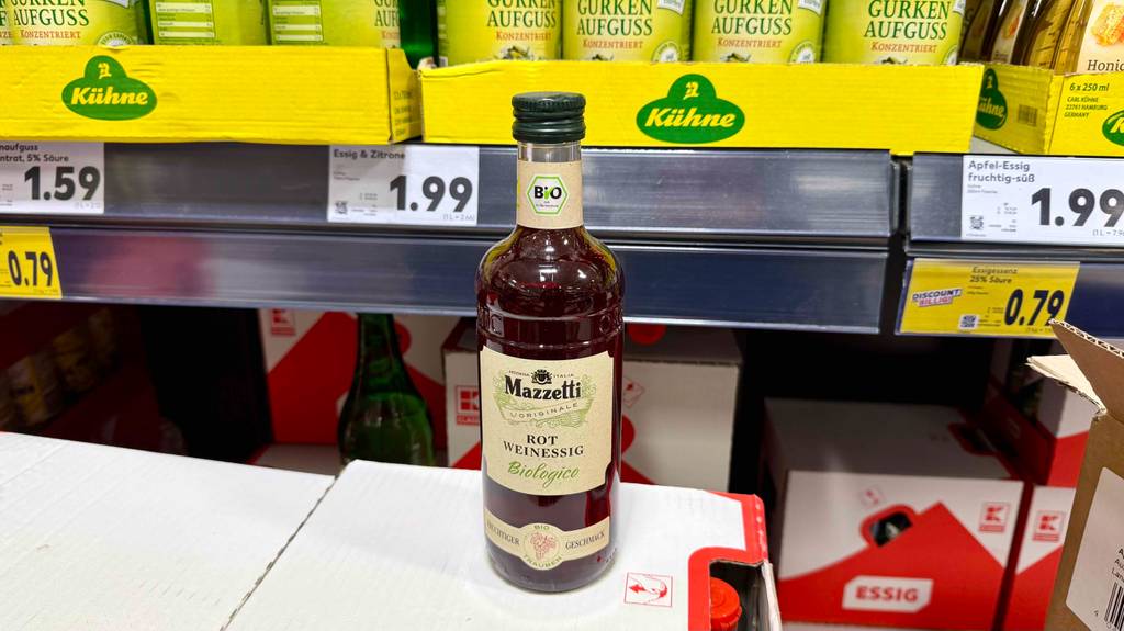 Rotweinessig im Test: Eine Flasche steht auf einem Karton vor einem Verkaufsregal.