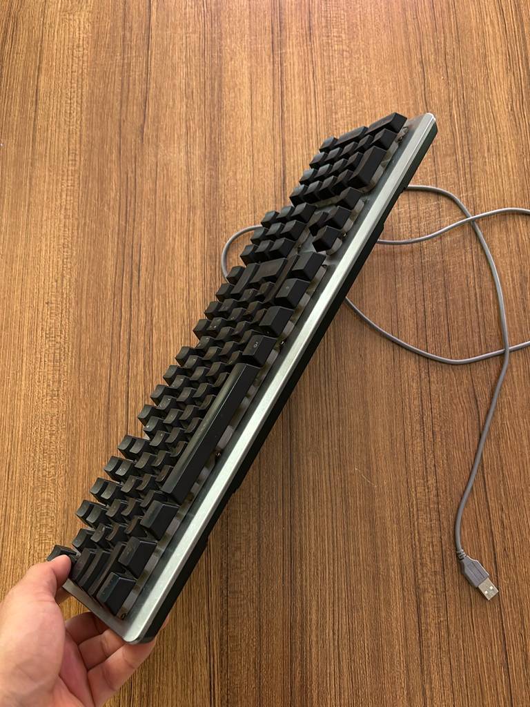 Vorderseite einer getesteten mechanischen Tastatur von einer Hand schräg gehalten auf einer Holzfläche.