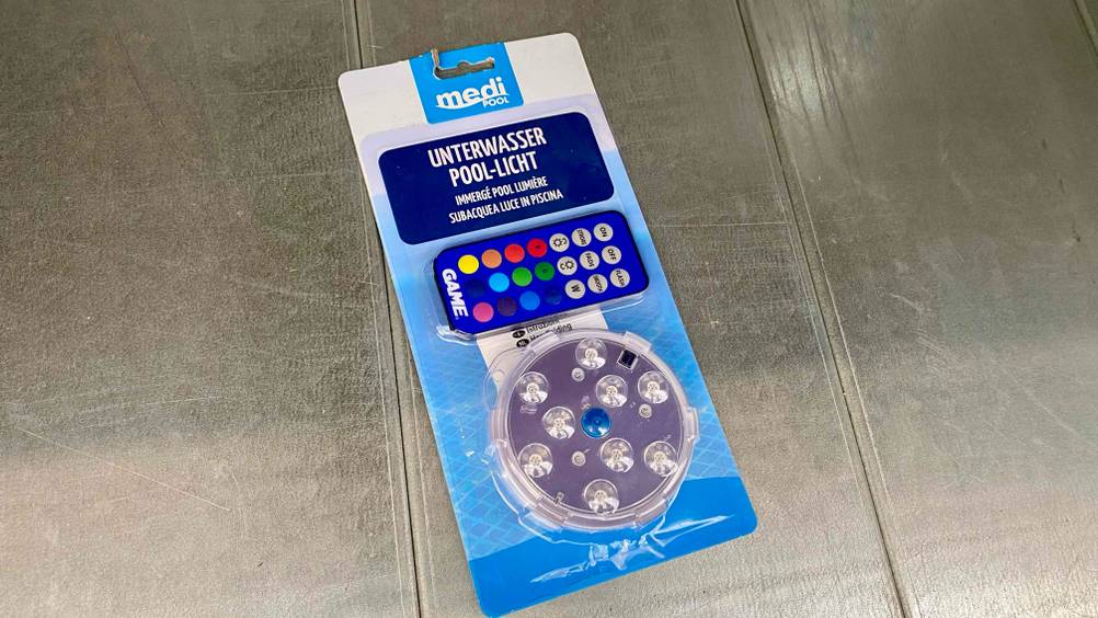Im Test: Eine originalverpackte Poolbeleuchtung inklusive Fernbedienung von oben auf einer Metallfläche.