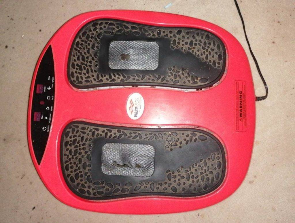 Ansicht von oben auf ein rotes getestetes Fußmassagegerät mit Vibration steht auf einem Zementboden.