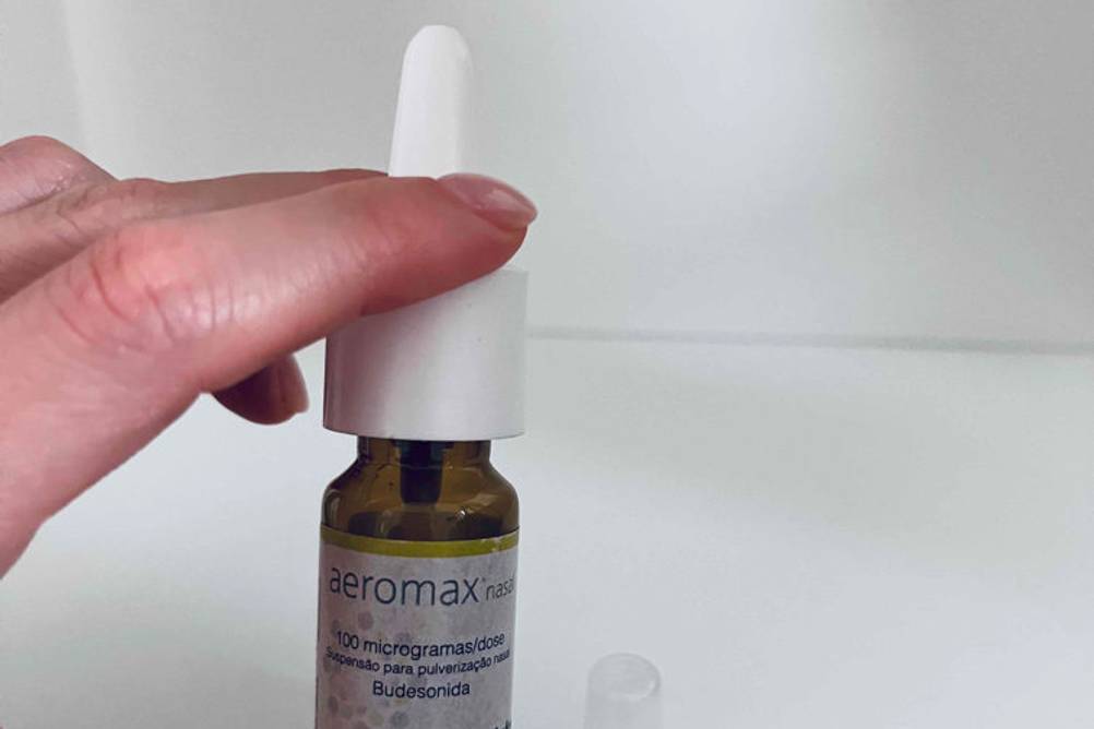 Hand hält kleinen geöffnten Flacon mit getestetem Allergie-Nasenspray von Medinfar vor weißem Hintergrund.