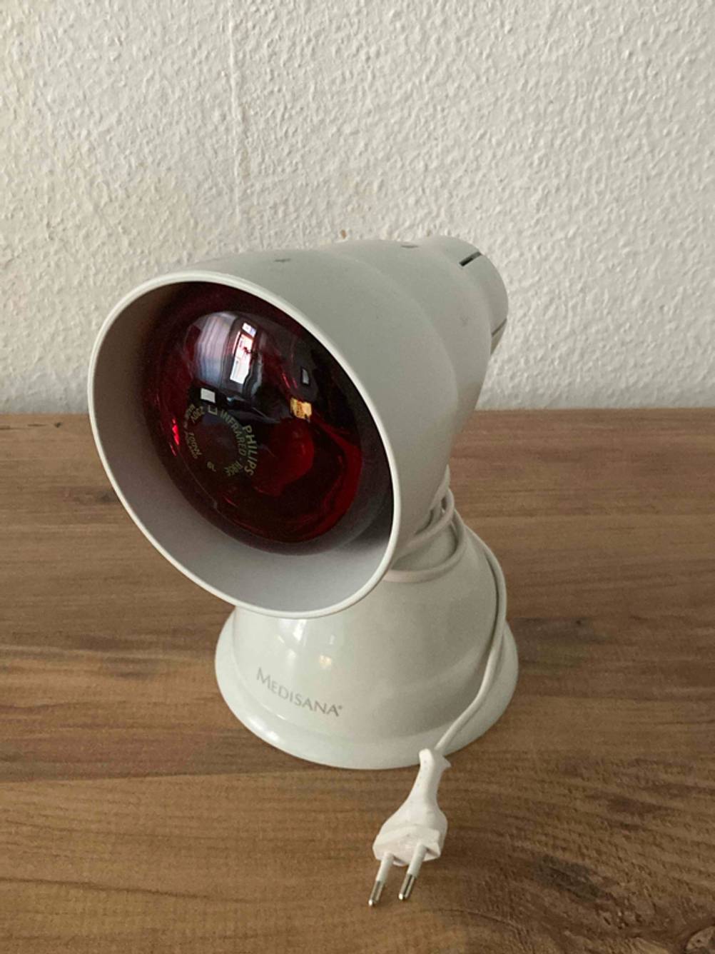 Eine Rotlichtlampe steht getestet mit aufgerolltem Stromkabel auf einem Holzboden.