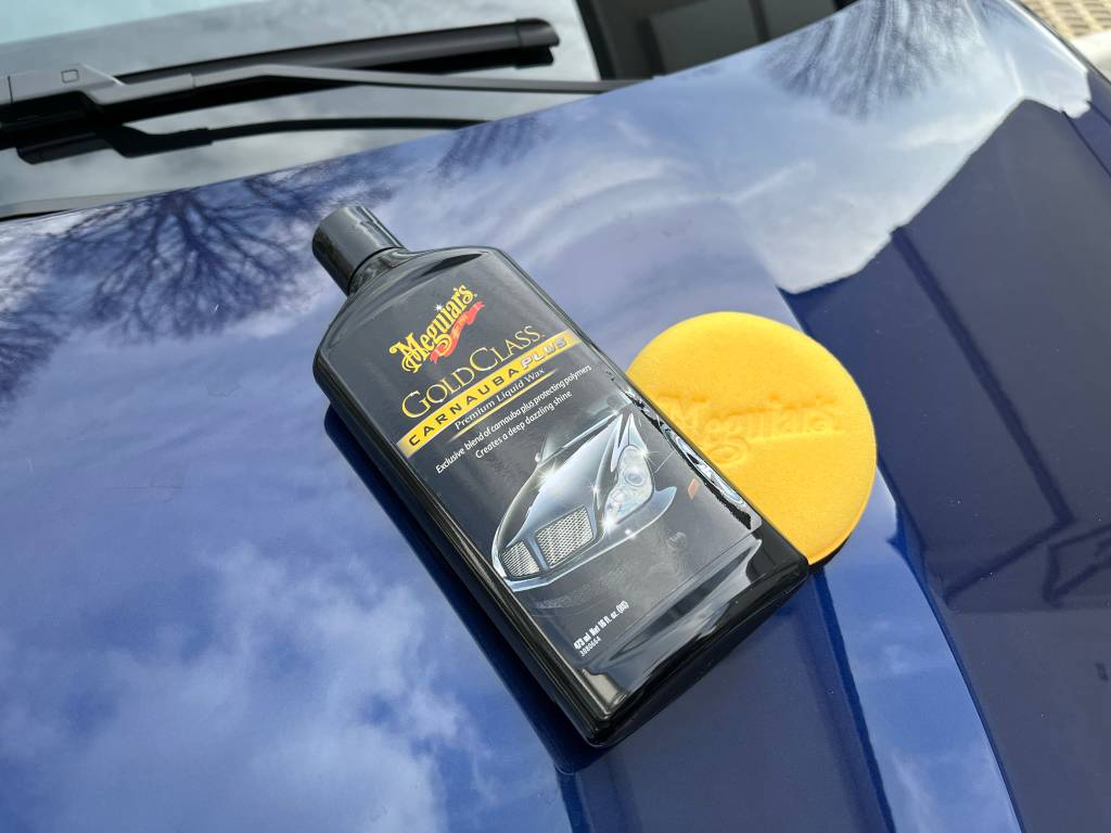 Eine Packung Autopolitur liegt auf der Motorhaube eines Autos, daneben ein Schwamm