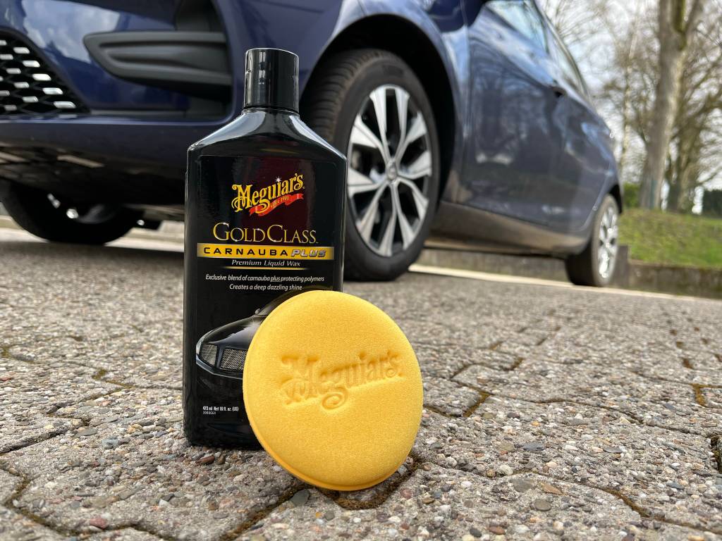 Eine Packung Autopolitur mit einem Schwamm vor einem schwarzen Auto stehend