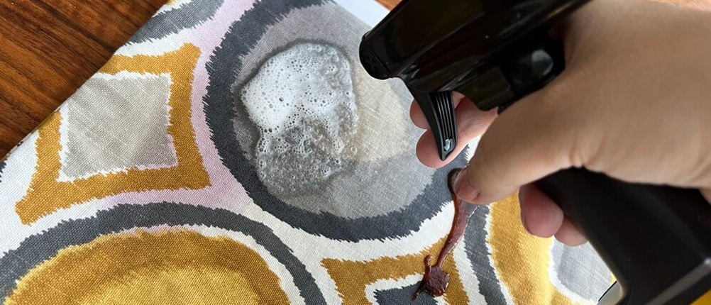 Eine Hand sprüht etwas von dem Meguiar's Polsterreiniger ME G9416 auf einen Kissenbezug.