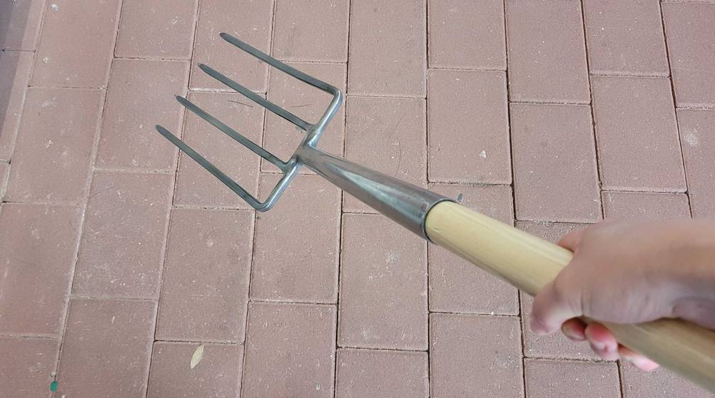 Eine Hand hält eine getestete Grabegabel vor eine Steinfläche.