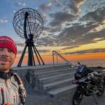 Meli Schönbrodt, VGL-Experte für Motorräder, mit seinem Motorrad vor einem Landmark, dahinter untergehende Sonne.
