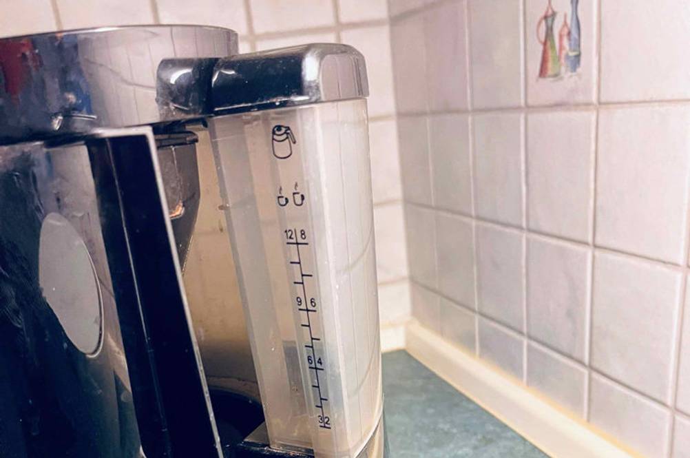 Im Test: Teilansicht mit Tassenangabe einer schwarzen Kaffeemaschine mit Direktbrühsystem, die auf einem blauen Untergrund vor weißen Fliesen steht.