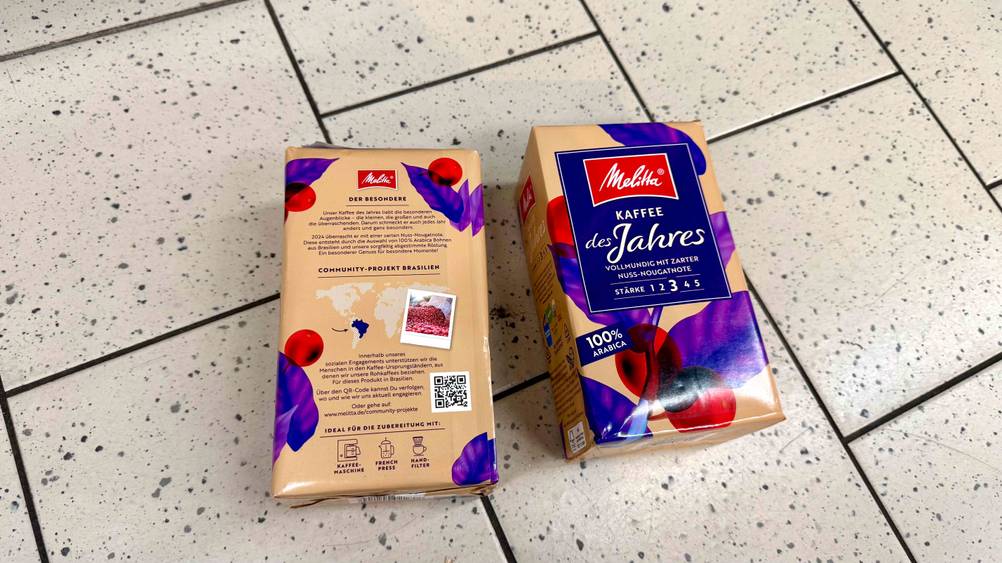 Zwei Packungen des Melitta-Kaffees im Test auf einem Boden liegend, eine mit der Vorderseite nach oben, die andere mit der Rückseite.