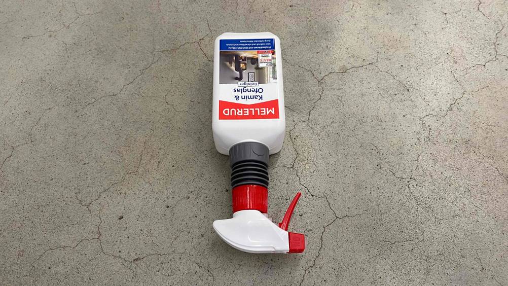 Getesteter Mellerud-Kaminreiniger liegt kopfunter in einer Sprühflasche auf grauem Untergrund.
