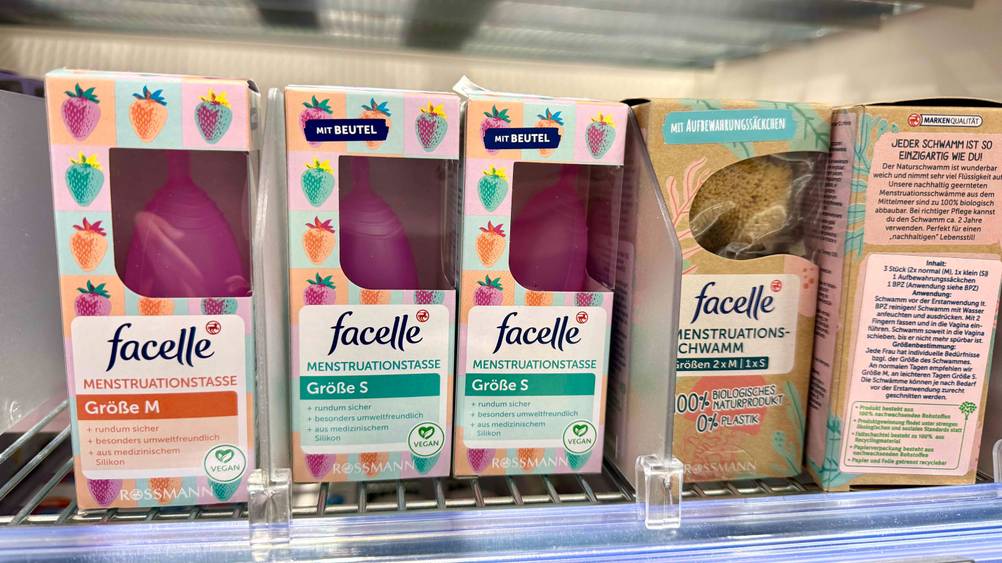 Mehrere Packungen der getesteten Menstruationstasse in einem Verkaufsregal neben anderen Produkten.