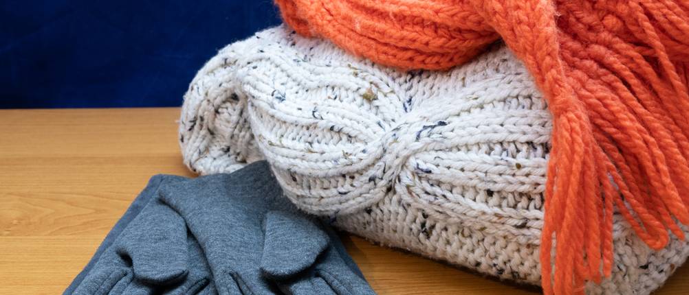 Merino-Handschuhe im Test: Ein Paar grau-blaue Merino-Handschuhe liegen neben einem Wollpullover und einem Wollschal auf einem Holztisch.