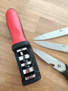 Ein Messerschärfer im Test steht neben Messern und Scheren auf einer Holzfläche, von oben betrachtet.