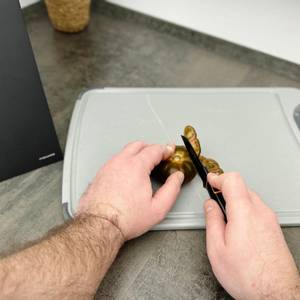 Ein Messer aus dem Fiskars-6424009787917-Set schneidet eine Tomate auf einem Kunststoffbrett. Die Hände führen den Schnitt präzise.