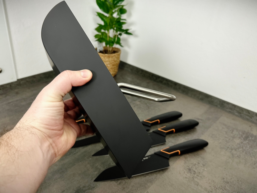 Der Messerblock Fiskars 6424009787917 wird seitlich gehalten und zeigt den Griffbereich zur Wandmontage. Im Hintergrund liegen die zugehörigen Messer auf der Arbeitsfläche.