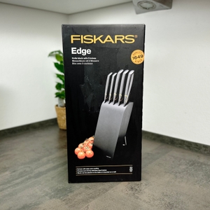Die Vorderseite der Produktverpackung des Fiskars 6424009787917 zeigt ein Foto des Messerblocks mit Tomaten im Vordergrund. Oben steht der Markenname in Gelb.
