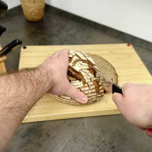 Ein Brotlaib wird mit einem gezahnten Brotmesser aus dem WMF-1874699990-Set geschnitten. Das Messer wird flach geführt.