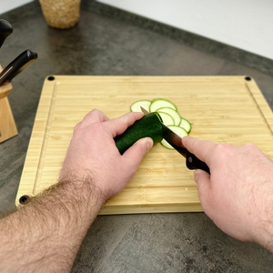 Eine Gurke wird auf einem Schneidebrett mit einem WMF-Messer in Scheiben geschnitten. Die Hände führen die Klinge entlang der Gemüsesorte.